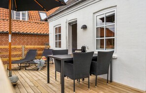 Une terrasse avec une table et des chaises, un mur en briques et un bâtiment blanc doté de fenêtres.