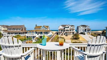 A balcony with white Adirondack chairs, a table with drinks, and a view of beachfront houses.