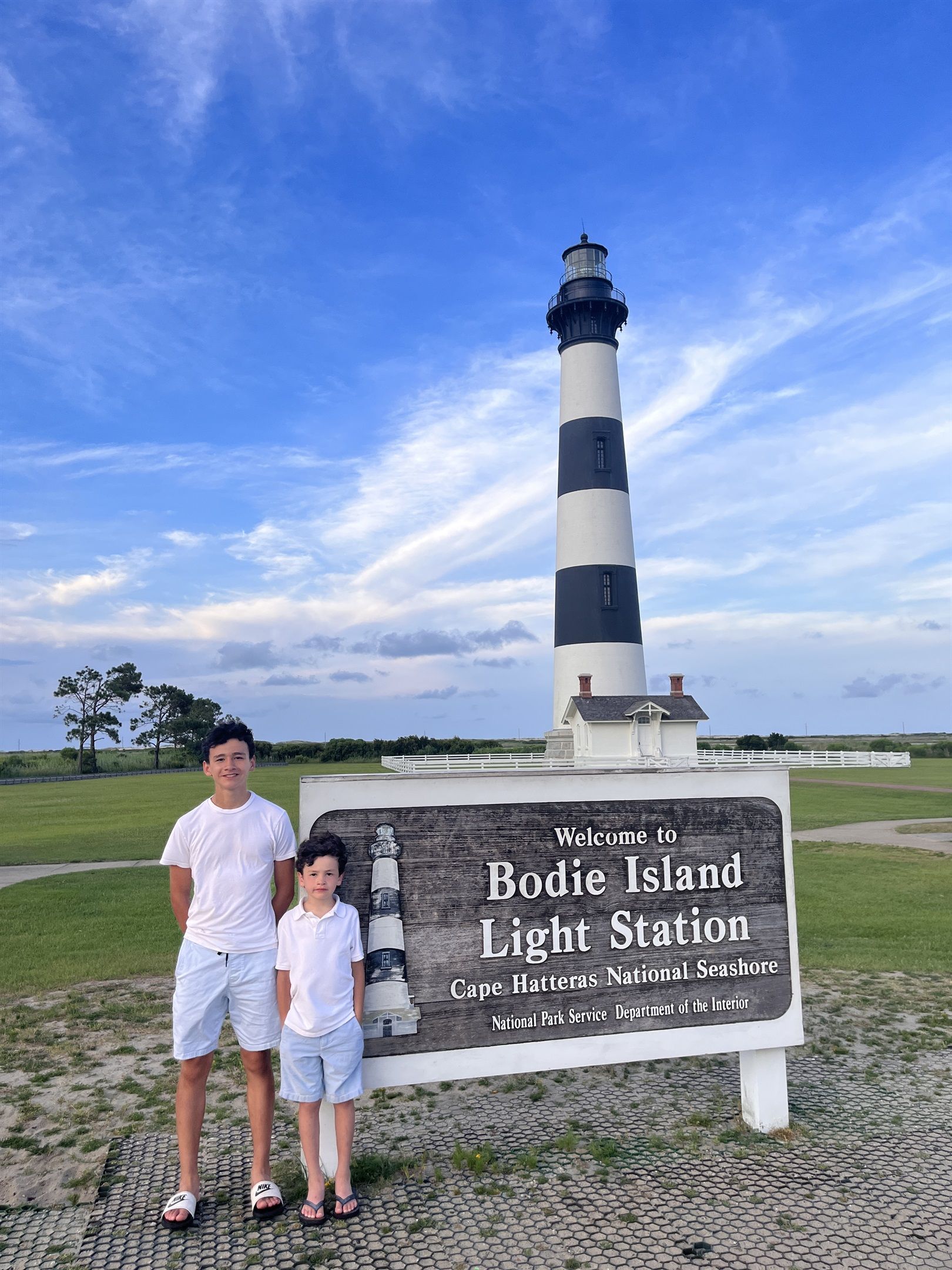 A lighthouse with a sign reading 'Welcome to Bodie Island Light Station Cape Hatteras National Seashore Department of the Interior National Park Service.'