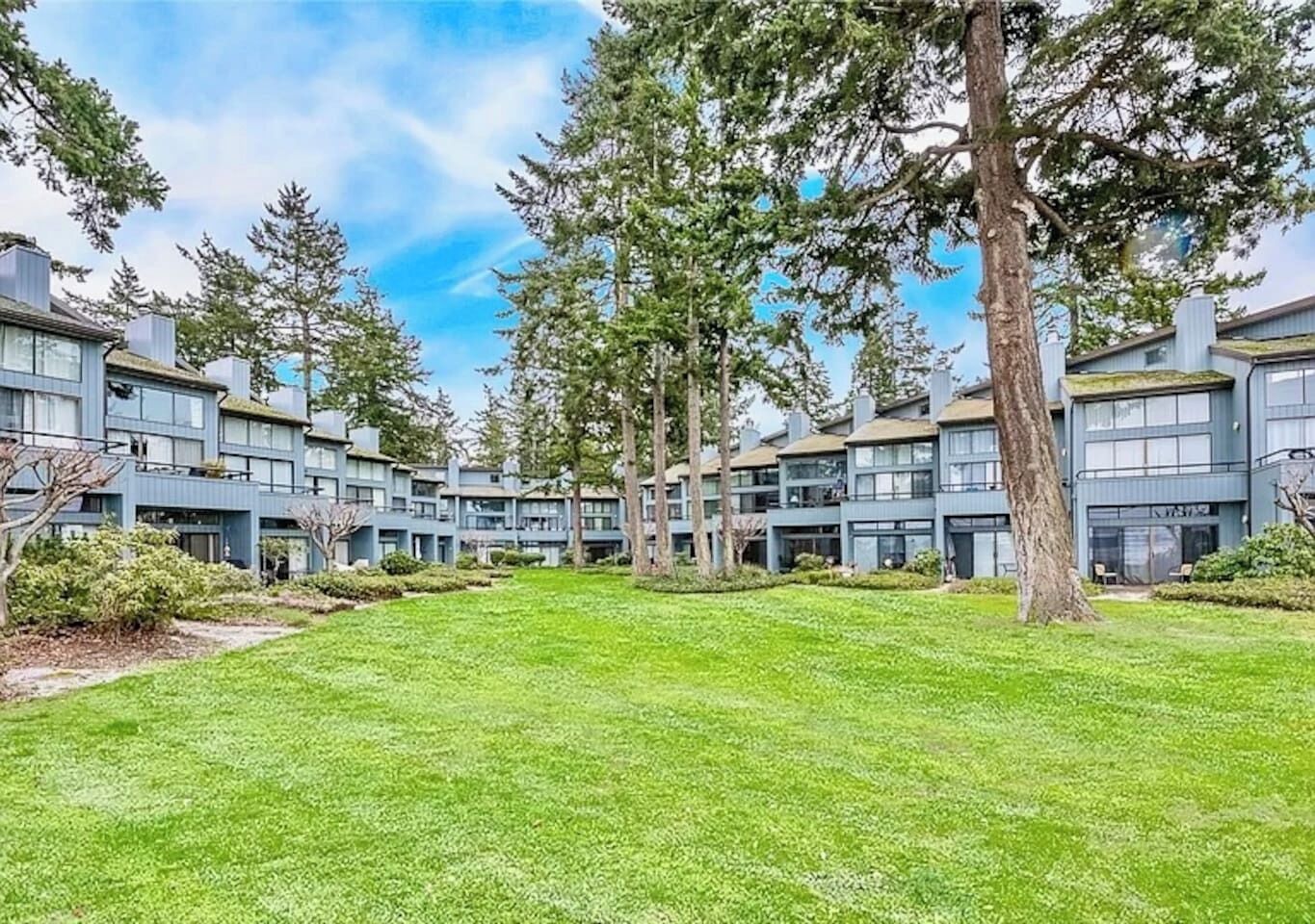A modern apartment complex with multiple buildings, a well-maintained lawn, and mature trees.