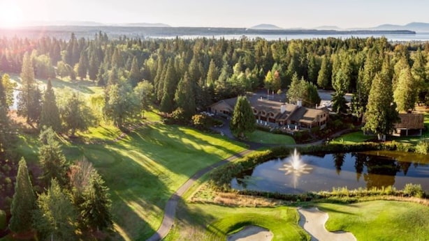 A golf course with a pond, a walking path, and a building with multiple rooms.