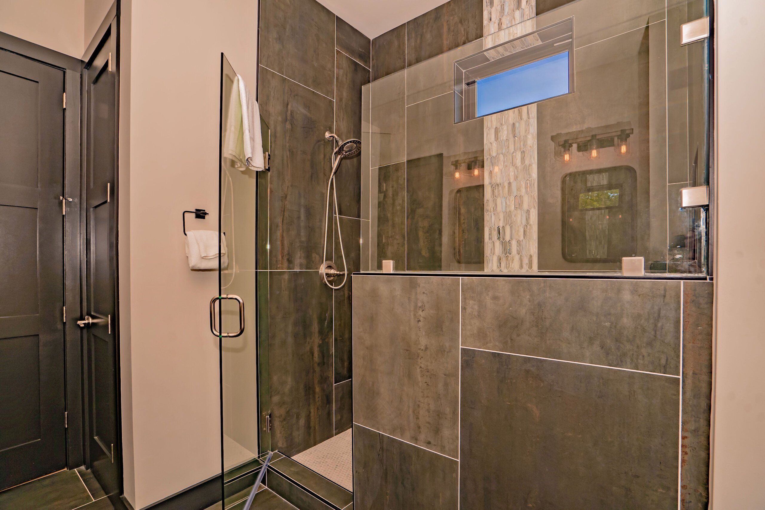 A modern bathroom with a glass shower enclosure, a large mirror, and a door with a towel rack.