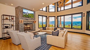 A spacious living room with a fireplace, large windows, and a view of the mountains. - Manna Mountain Lodge ~  Indoor Pool, XBox Room, Gaming Garage, Views & More! (Sevierville)
