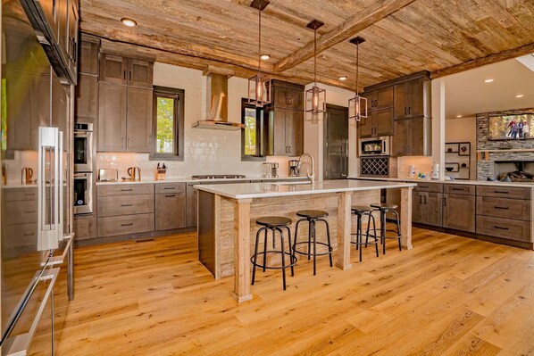 Una cocina moderna con suelo de madera, una isla central con taburetes, electrodomésticos de acero inoxidable y una chimenea de piedra.