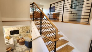 A modern staircase with wooden steps and black metal railings, leading to a second-floor living area with a stone fireplace, a sofa, and a coffee table. - Mid-Century Retreat Overlooking the Pines & Pacific (Cambria)