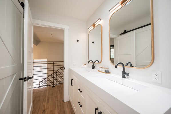 A modern bathroom with two sinks, a large mirror, and a wooden staircase leading to another room. - Mid-Century Retreat Overlooking the Pines & Pacific (Cambria)