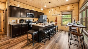 A modern kitchen with dark wooden cabinets, stainless steel appliances, and a central island with bar stools. - 3 Miles to Pigeon Forge Parkway! Private Pool 🏊‍♂️ Hot Tub 🐕 Dogs 🏔️ GSMNP Views 🌄 (Sevierville)