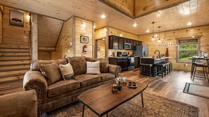 A cozy cabin interior with a wooden interior, a sofa, a coffee table, and a kitchen area. - 3 Miles to Pigeon Forge Parkway! Private Pool 🏊‍♂️ Hot Tub 🐕 Dogs 🏔️ GSMNP Views 🌄 (Sevierville)