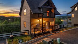 A two-story house with a porch, a fenced yard, and a view of a road and hills. - 3 Miles to Pigeon Forge Parkway! Private Pool 🏊‍♂️ Hot Tub 🐕 Dogs 🏔️ GSMNP Views 🌄 (Sevierville)