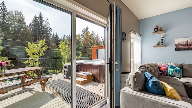 Una sala de estar moderna con un puerta corrediza de vidrio que da a un balcón con jacuzzi y una mesa de picnic de madera.