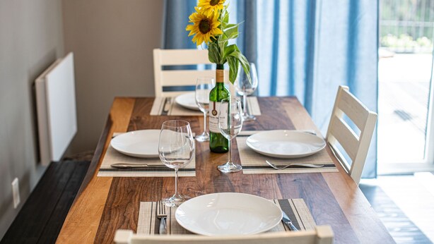 Une table à manger dressée avec des assiettes, des verres à vin et une bouteille de vin, et un vase rempli de tournesols placé au centre.