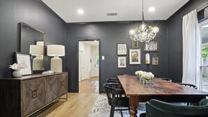Uma sala de jantar com uma mesa de madeira, cadeiras pretas, um armário de madeira escura e um lustre.