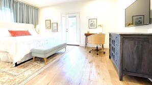 Um quarto com cama, escrivaninha, cadeira, cômoda e porta.
