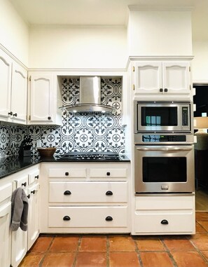 A kitchen with white cabinets, a black and white patterned backsplash, a stove, and a microwave.
