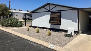 A single-story mobile home with a gabled roof, a small attached garage, and a gravel driveway. - Fun Rustic 2/2 Single level in a great community. (Laughlin)