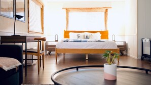 Ett modernt hotellrum med en säng i trä, ett skrivbord och ett runt bord med en växt.