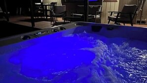Ett bubbelbad med blått ljus, omgivet av utemöbler och en tv-skärm i bakgrunden.