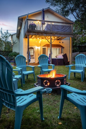 A backyard with a fire pit, outdoor seating, and a house with a balcony.