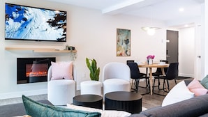 Un salon moderne doté d’une cheminée, d’un téléviseur à écran plat, d’un coin repas et d’un grand tableau abstrait.