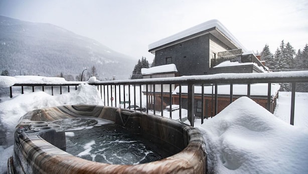 Un bain à remous entouré de neige, avec un bâtiment en arrière-plan.