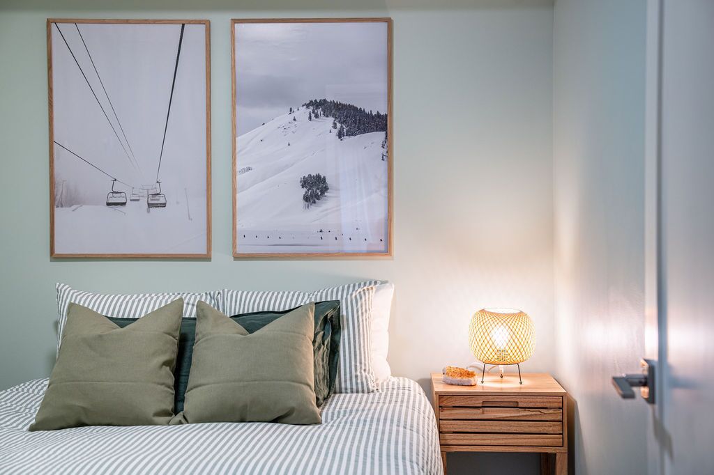 A bedroom with a bed, pillows, a nightstand with a lamp, and two framed pictures on the wall.