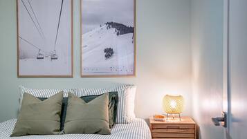 A bedroom with a bed, pillows, a nightstand with a lamp, and two framed pictures on the wall.