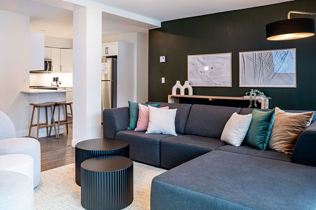 A modern living room with a grey sectional sofa, a coffee table, and a dining area with a kitchen in the background.