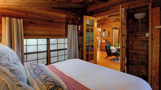 Un dormitorio de cabaña rústica con una cama grande, techo de madera y vista a la habitación contigua.