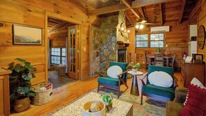 Interior acogedor de una cabaña de troncos con paredes de madera, una chimenea de piedra y dos sillones tapizados en verde.