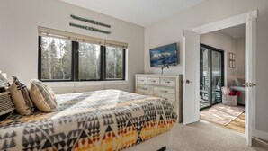 Un dormitorio con una cama grande, un aparador, un cuadro y vistas al exterior a través de una puerta.
