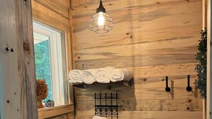 Un baño con paneles de madera, un inodoro, una lámpara colgante y un estante con toallas.