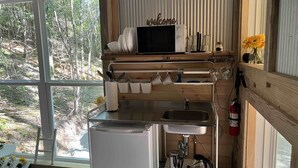 Cocina compacta con un lavamanos, refrigerador y cafetera. Una ventana ofrece vistas al exterior.
