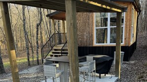 Una terraza de madera con mobiliario exterior, una escalera y vistas a zona boscosa.