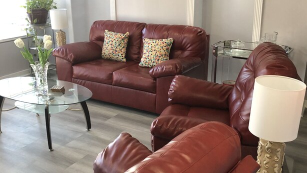 Un salon avec un canapé en cuir marron, deux fauteuils assortis, une table basse en verre et une lampe décorative.