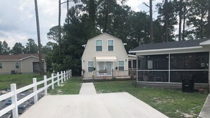 Il s’agit d’une propriété résidentielle dotée d’un patio couvert, d’une clôture blanche et d’une allée en gravier menant à une maison avec un porche à l’avant.