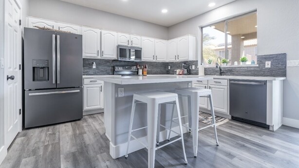 Una cocina moderna con armarios blancos, electrodomésticos de acero inoxidable y una isla central con taburetes de bar.