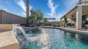 Piscina con cascada, rodeada de palmeras y un pérgola.
