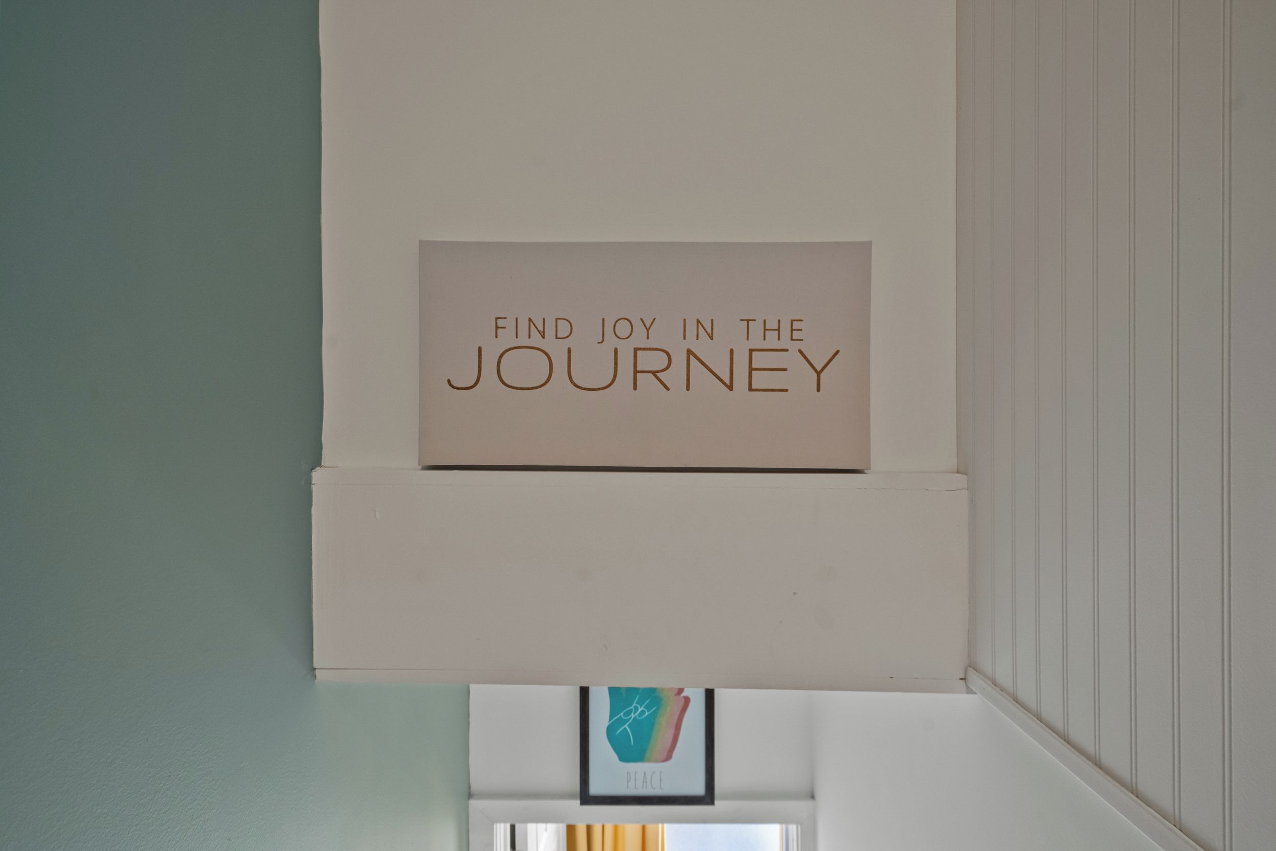 Eine Wand mit einem Schild, das 'FIND JOY IN THE JOURNEY' zeigt, und einem darunterhängenden Bild.