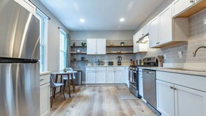 A modern kitchen with white cabinets, stainless steel appliances, and a wooden floor.