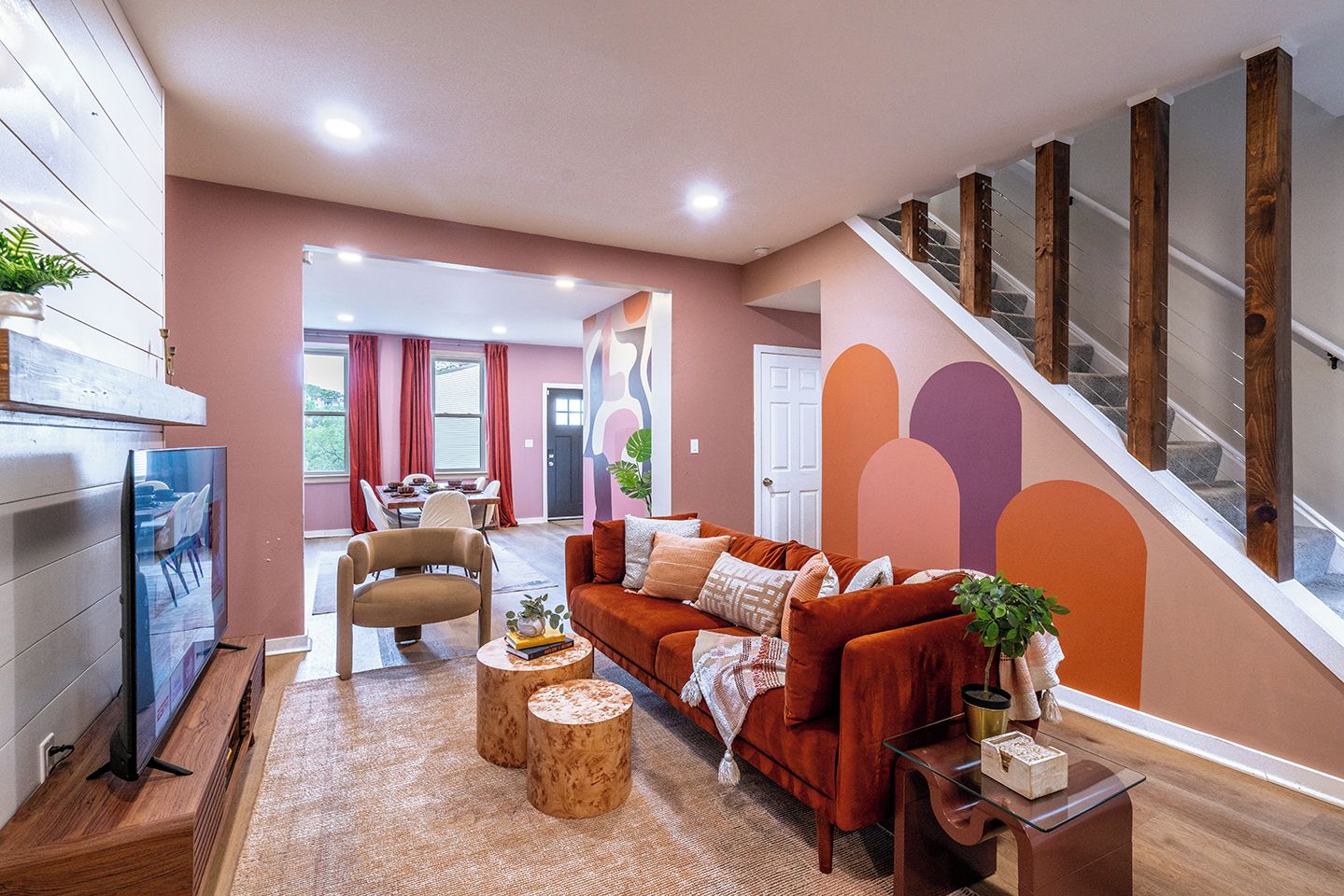 A modern living room with a sofa, coffee table, and TV. A staircase with wooden railings is visible.