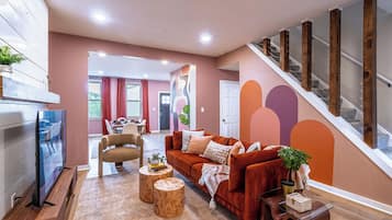 A modern living room with a sofa, coffee table, and TV. A staircase with wooden railings is visible.
