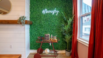 A room with a green wall, a #nomakeup sign, a small table with a book and glasses, and a window with red curtains.