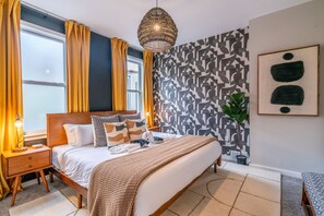 Un dormitorio moderno con cama, mesitas de noche, lámpara, pared con estampado geométrico y una lámpara colgante.
