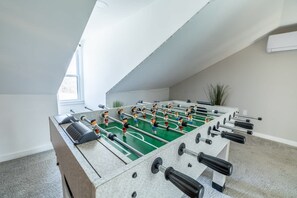 A foosball table in a room with a sloped ceiling, a window, and a plant. - Hot Tub | 2 King Beds | Parking | Family Friendly (Pittsburgh)