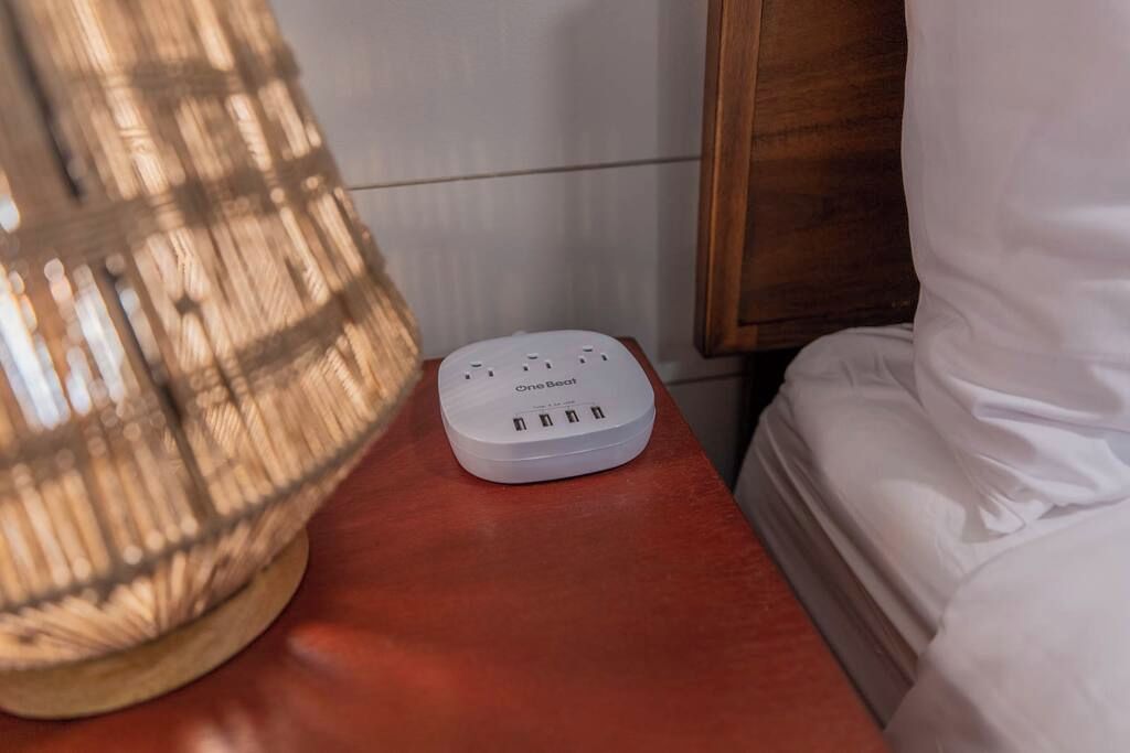 Un dispositivo OneBeat bianco su un comodino di legno, vicino a una lampada e un letto.