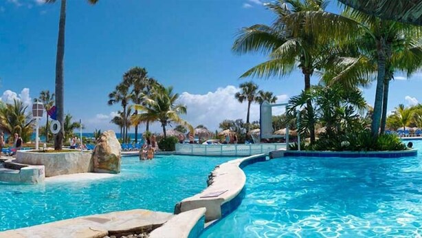 A resort pool area with clear blue water, palm trees, and a view of the ocean. -  Dream Holidays Vacation (Puerto Plata)