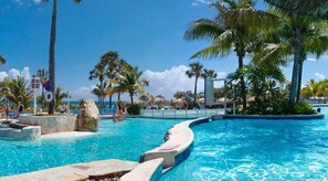 A resort pool area with clear blue water, palm trees, and a view of the ocean. -  Dream Holidays Vacation (Puerto Plata)
