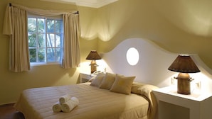 A bedroom with a bed, two bedside lamps, a window with curtains, and a view of palm trees. -  Dream Holidays Vacation (Puerto Plata)