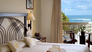 A hotel room with a bed, a nightstand, a lamp, a view of the ocean, and a balcony with chairs and a potted plant. -  Dream Holidays Vacation (Puerto Plata)