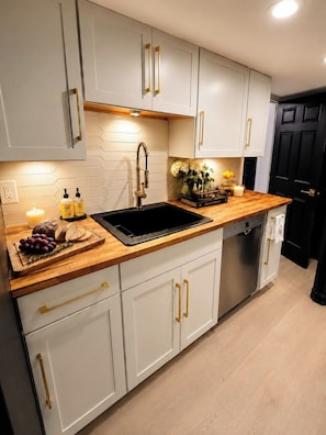Una cocina moderna con armarios blancos, un lavamanos negro y una encimera de madera.